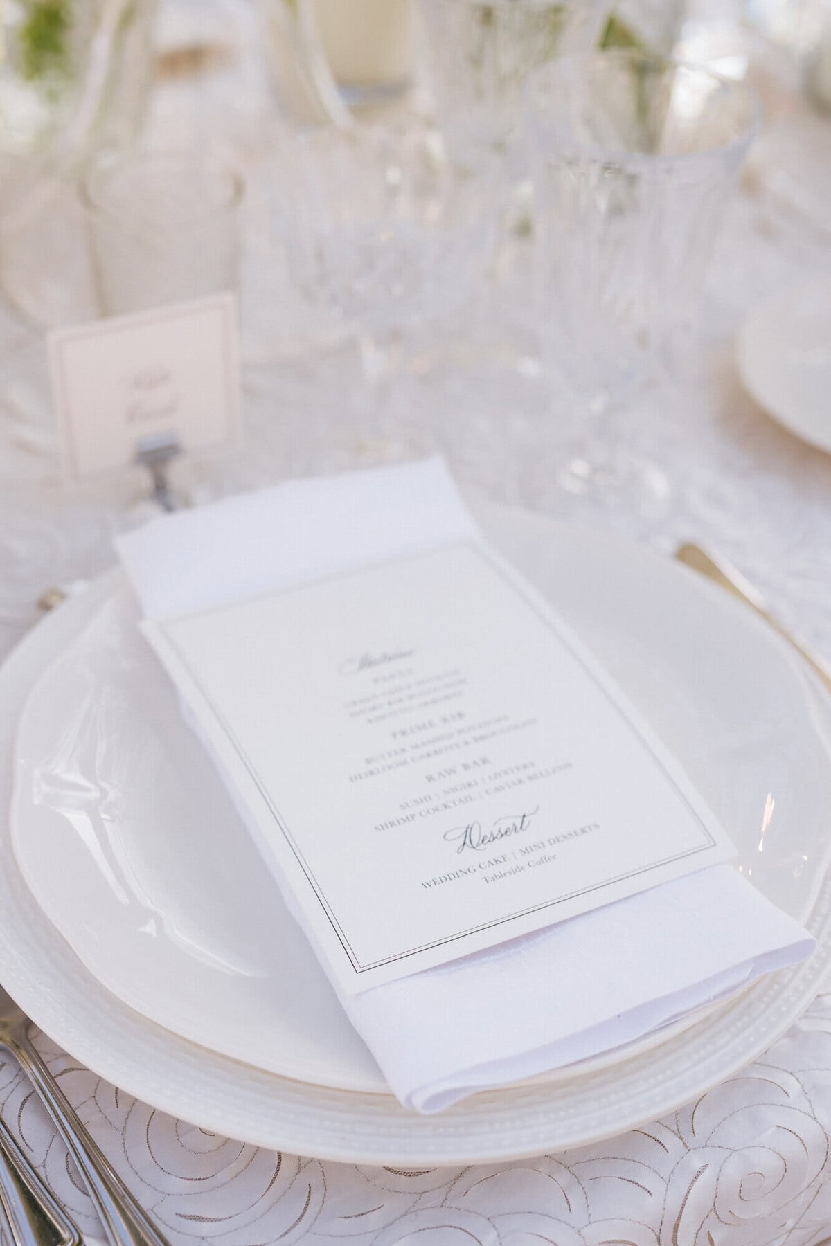 A close-up of a wedding menu displayed on an elegant white plate with crystal glassware at an Arizona Biltmore Scottsdale wedding, showcasing the fine details of the reception table design.