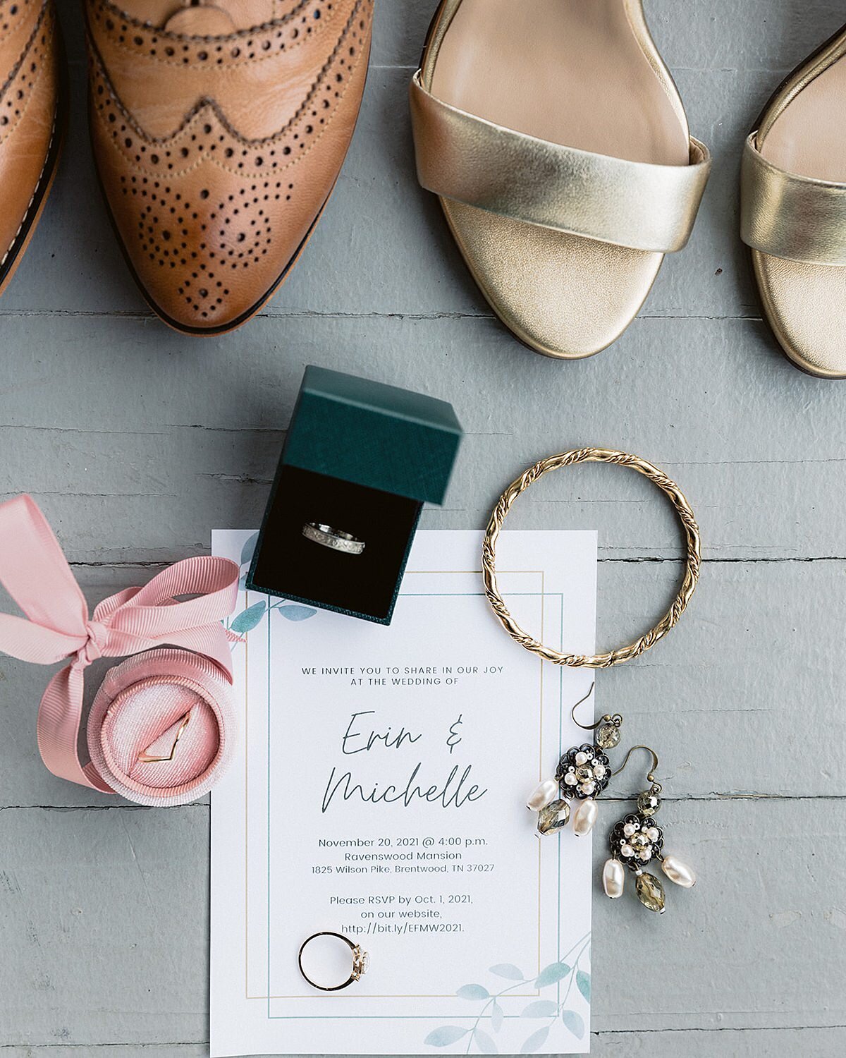 Detail image of wedding invitation for LGBTQIA wedding in Nashville. One pair of brown wingtip shoes sits next to a pair of gold satin sandals with a pink ring box holding a v shaped gold wedding band next to a dark green ring box holding a platinum wedding band. The wedding invitation with leaf details has an engagement ring and pair of pearl earrings for their wedding at Ravenswood Mansion in Nashville, TN