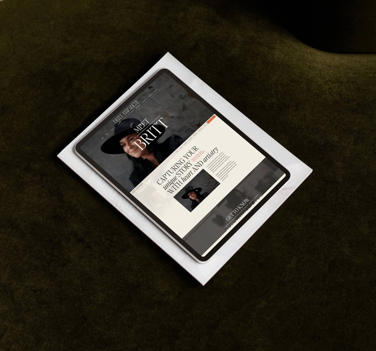 A tablet displays a website featuring portraits. The headline reads "Meet Britt," with additional text about capturing emotions in photos. The tablet, showcasing custom brand and Showit web design for photographers, rests on top of a white paper on a dark green surface.