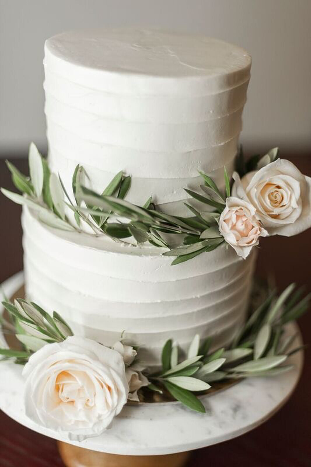 Classic 2 tiered white wedding cake with striped buttercream, topped with roses and greenery, by Lemonberry Pastries, contemporary cakes & desserts in Calgary, Alberta, featured on the Brontë Bride Vendor Guide.