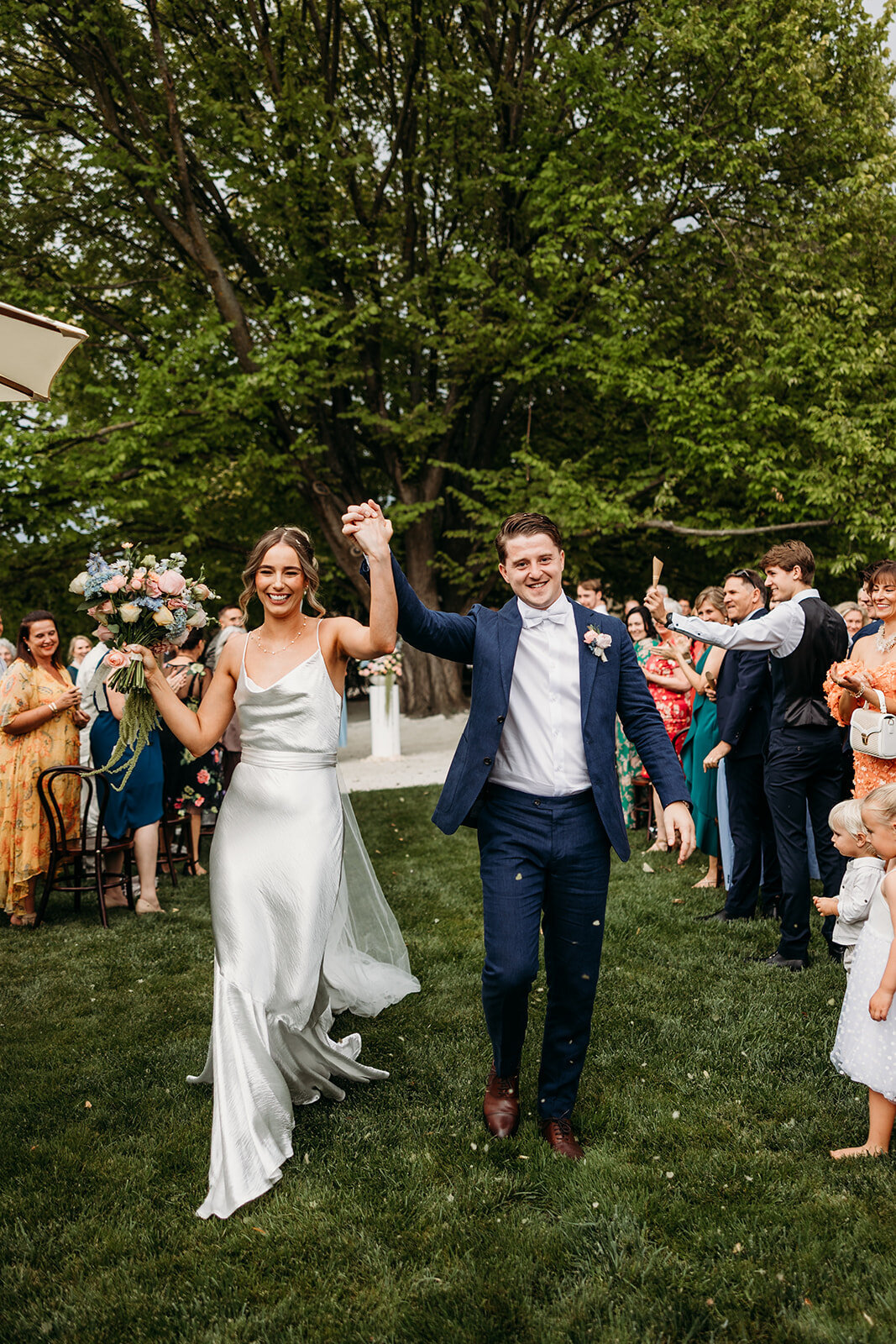 Bride and groom cheering as they exit their wedding ceremony on the homestead lawns at Poachers Pantry