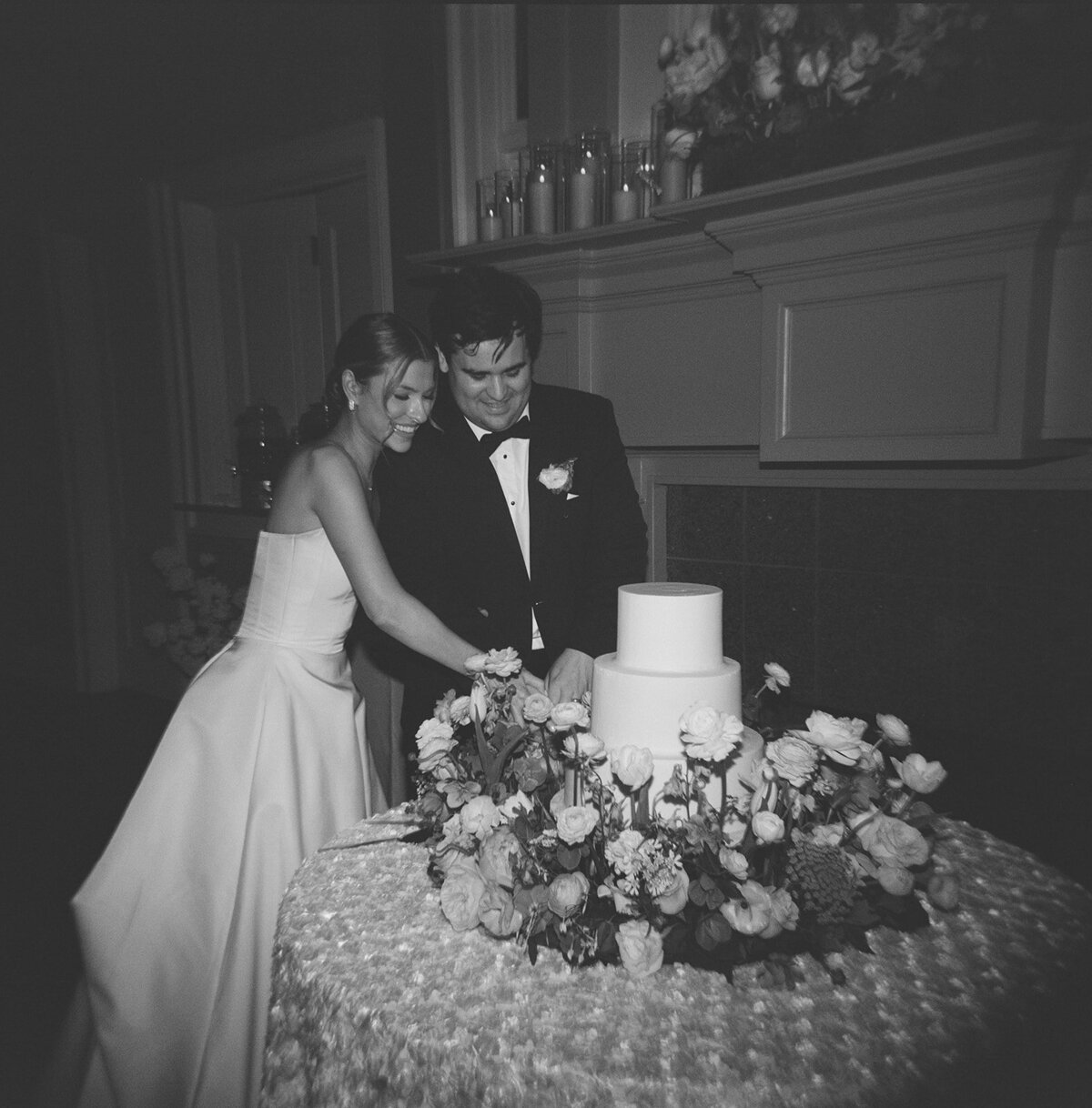 Bride and groom smiling as they cut their wedding cake together, captured in a timeless black and white film photograph at Burritt on the Mountain.