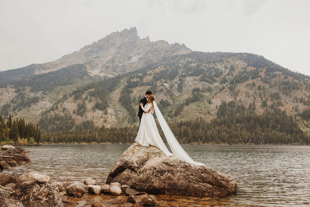 bride and groom kissing on large rock in lake