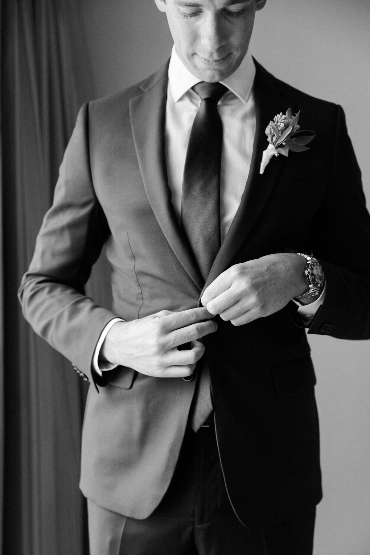 A close-up of the groom buttoning his suit jacket, his face partially visible as he focuses on adjusting his attire