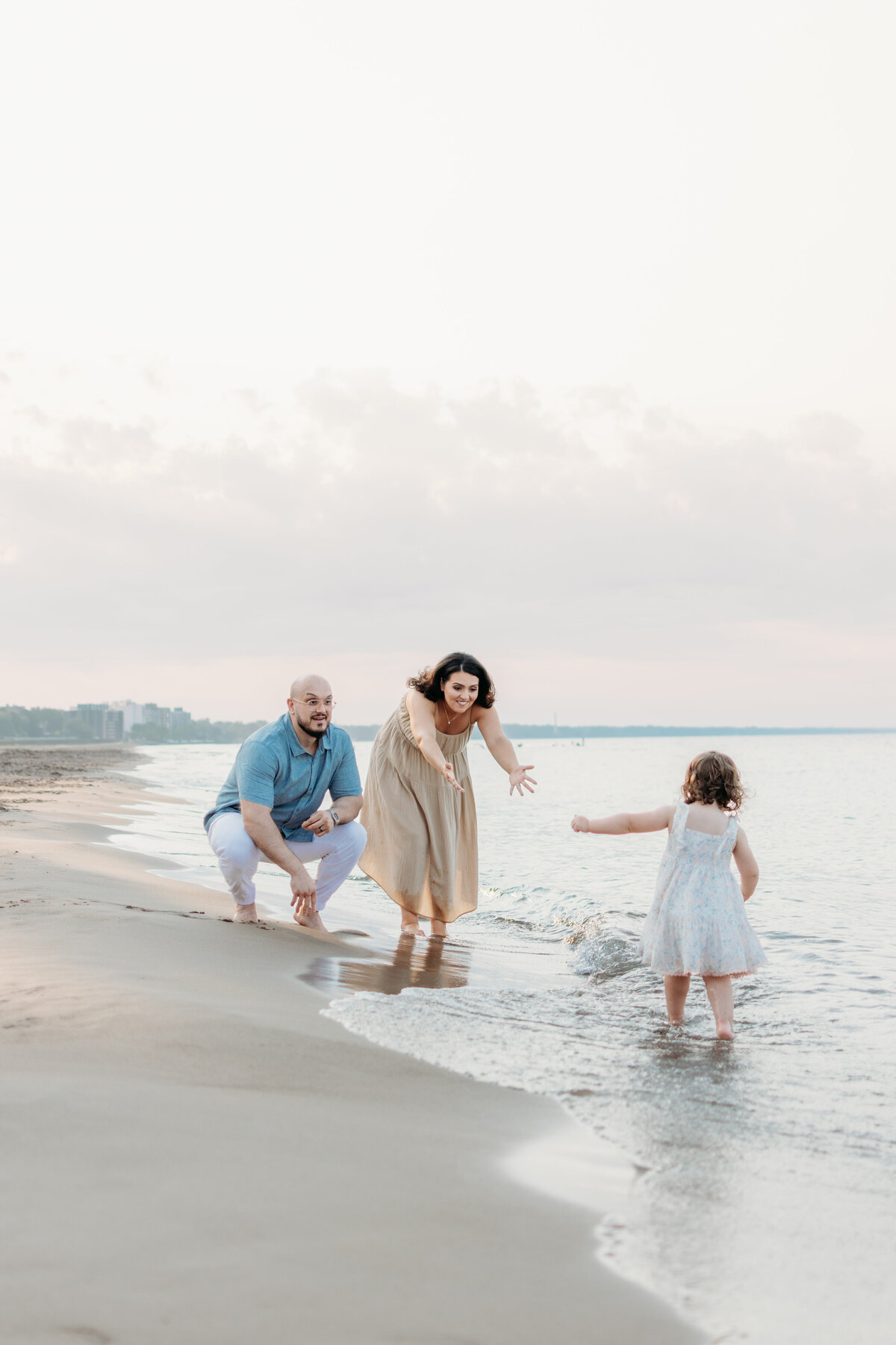 toddler girl running towards mom and dad by Lake Michigan