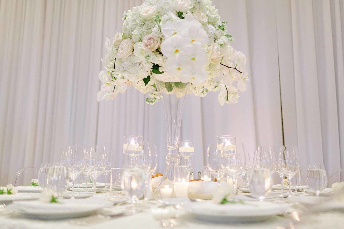 tall centerpiece of white hydrangea, white roses, and trailing white orchids, with candles at base