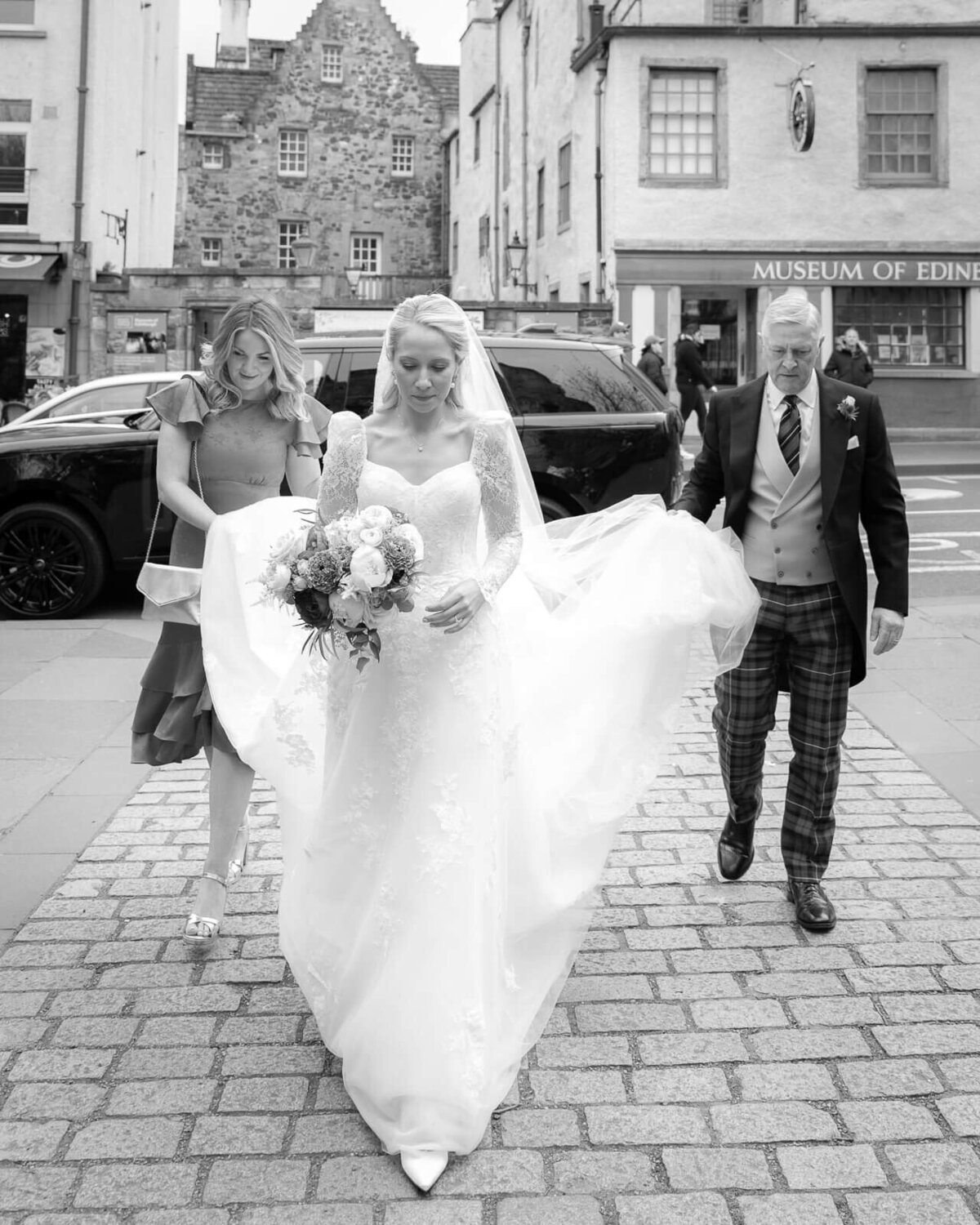 Bride with bridesmaid and father walk into church from their car in Edinburgh