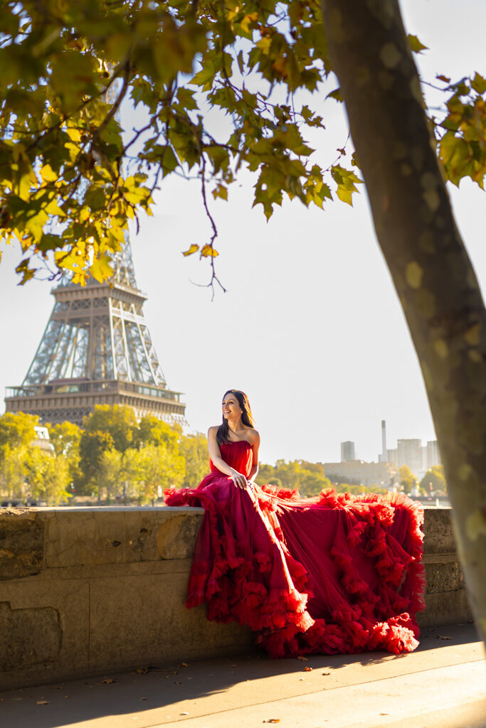 Classic Paris portrait featuring woman in red dress seated on wall with Eiffel Tower view