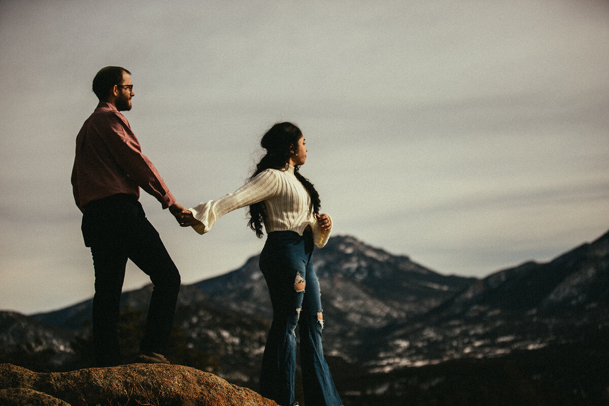 couple holds hands in front of rocky mountain national park 