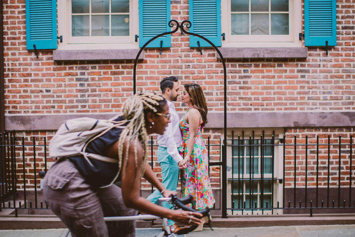 A couple standing under a metal arch on gay street with a bicyclist riding through in the village nyc