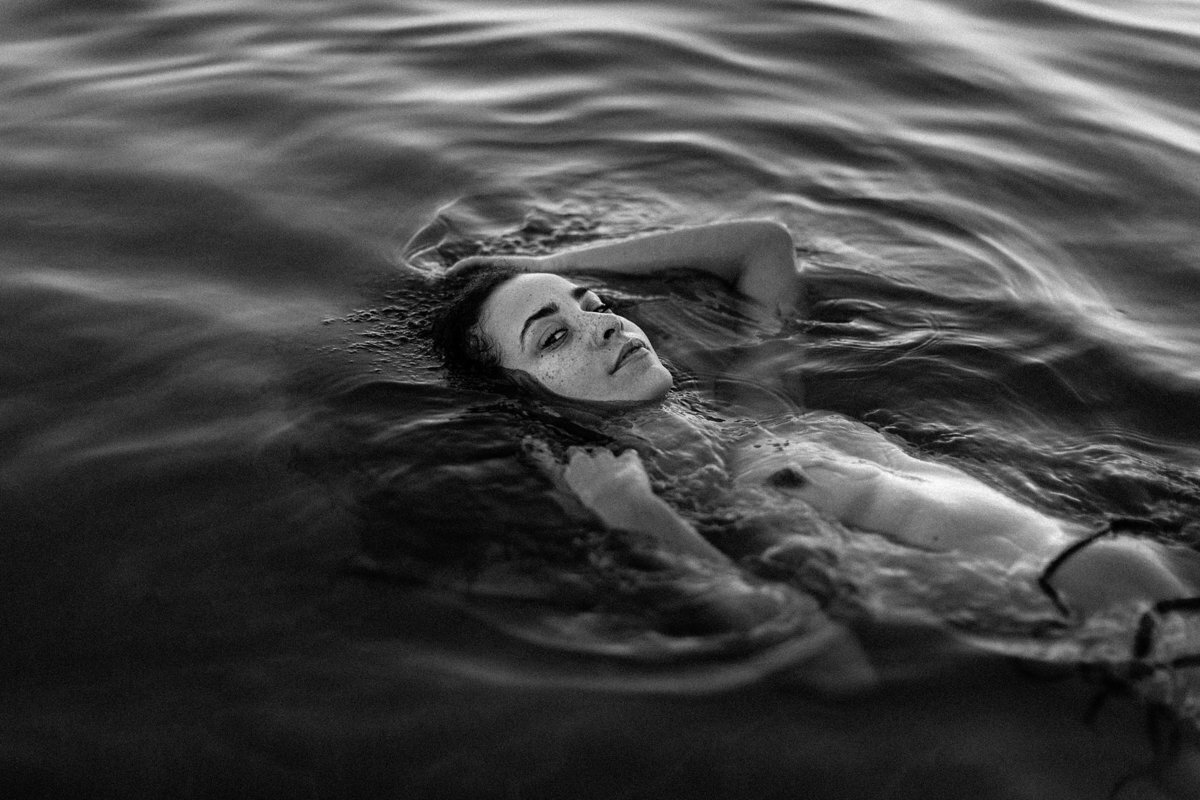 black and white photo of a person swimming in the water at sunset