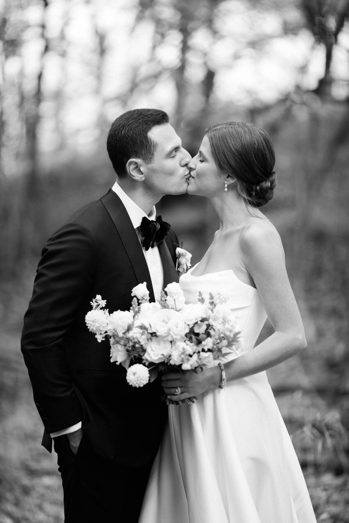 the bride and groom sharing a tender kiss, with the bride holding a full bouquet of white flowers