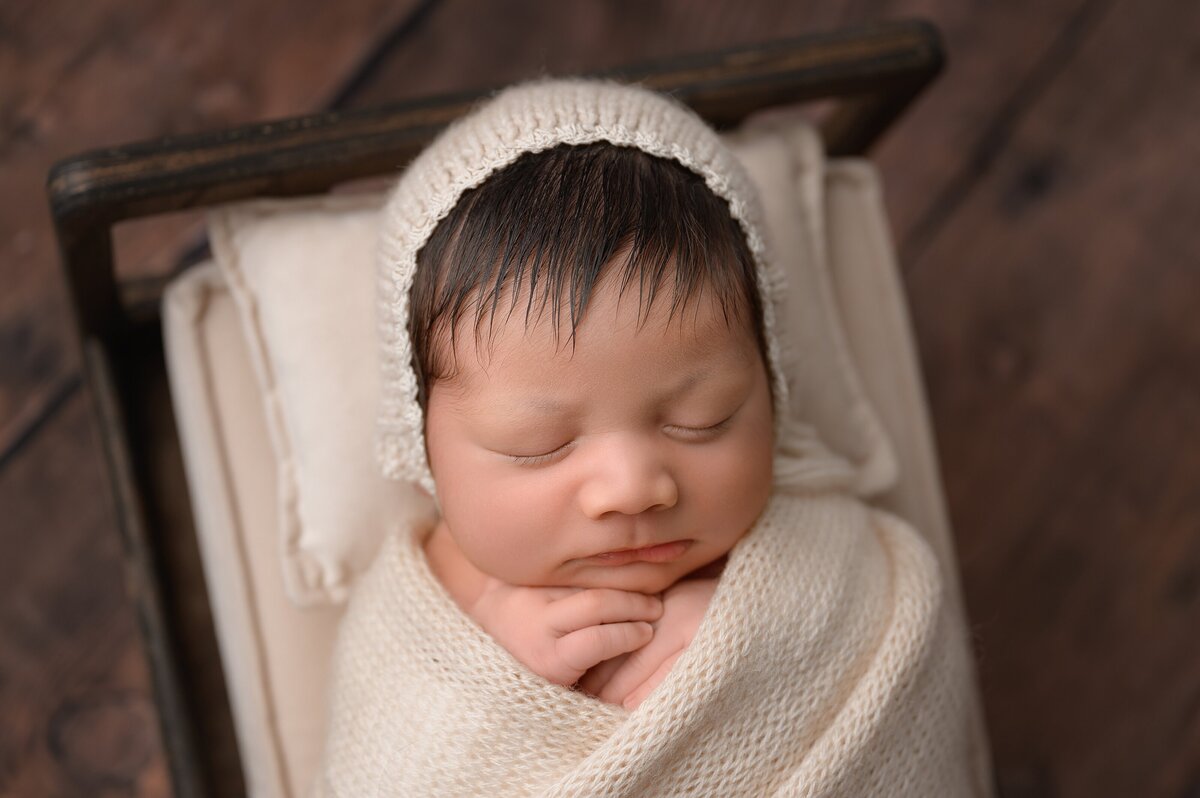 Baby boy newborn photographed in a little bed in very natural setting with neutral colors.