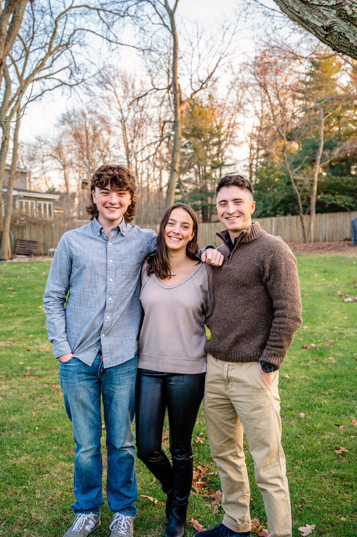 Three siblings - two brothers and a sister, young adults, standing next to each other posing for a family session outside.