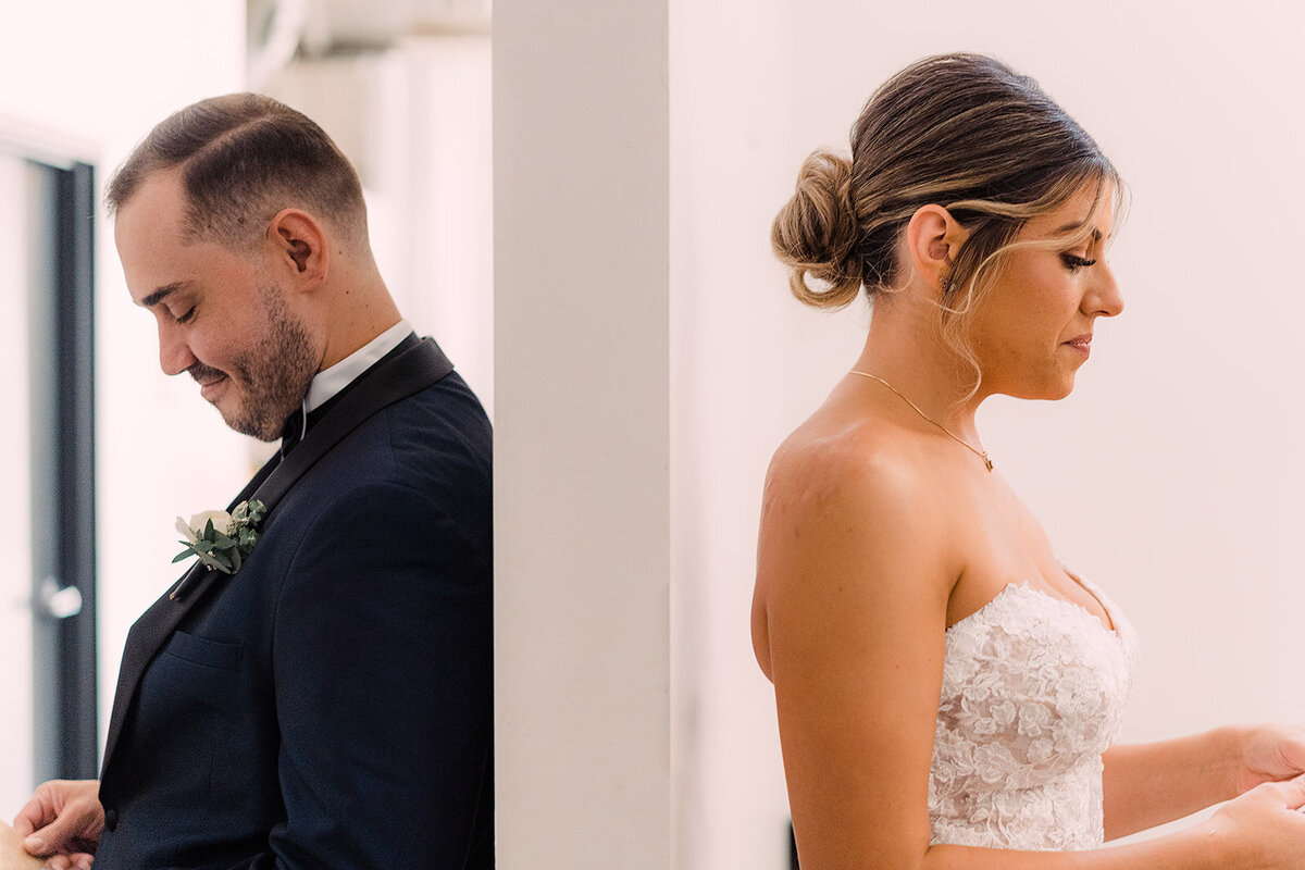 Bride and groom stand back-to-back on either side of a wall, reading private letters to each other with serene expressions.