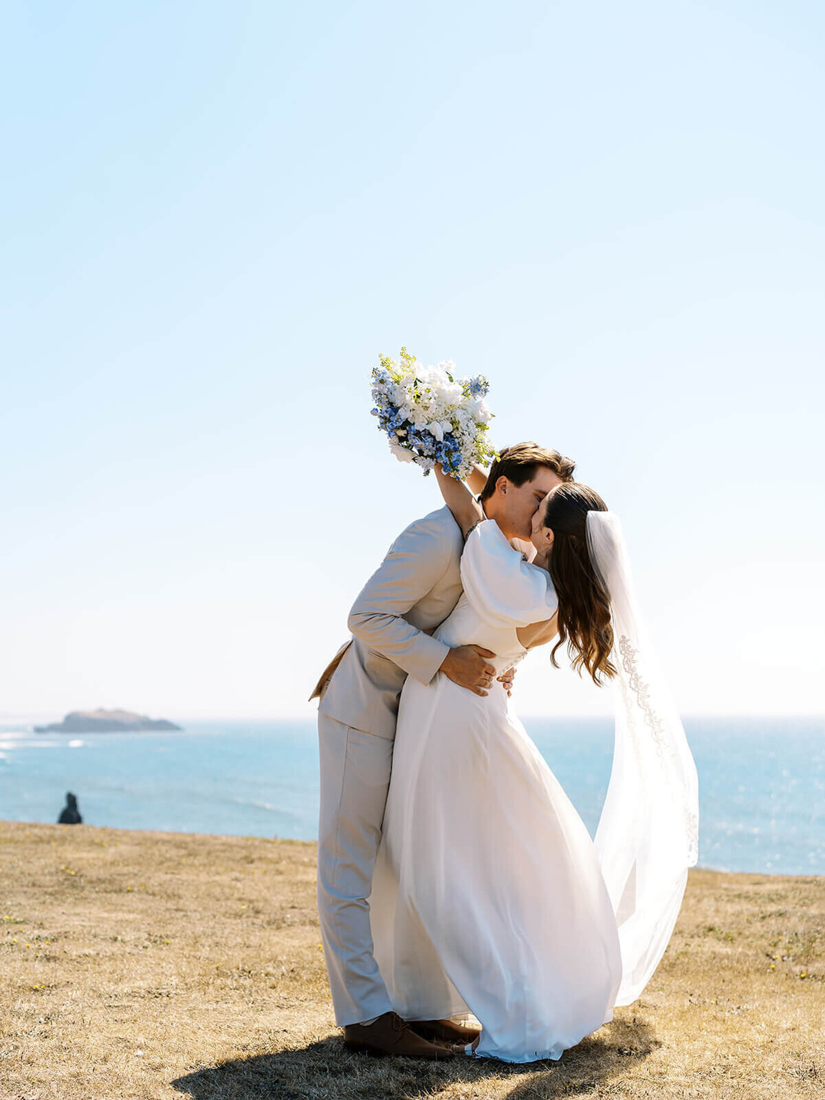 Bride and groom kissing with the ocean in the background.