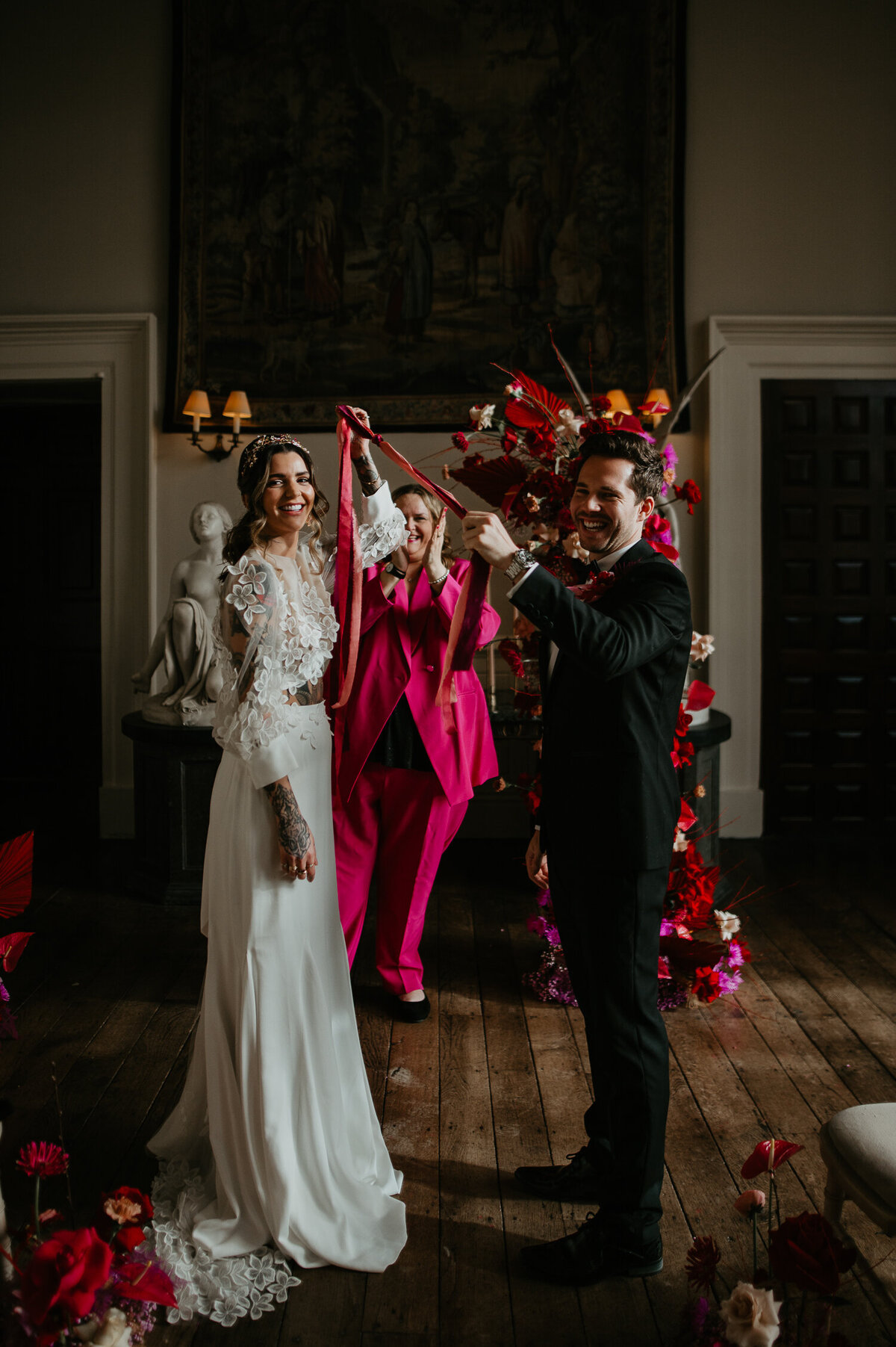 A hand fasting ceremony at Elmore Court between a young couple. The flowers are pink and the celebrant is wearing a pink suit.