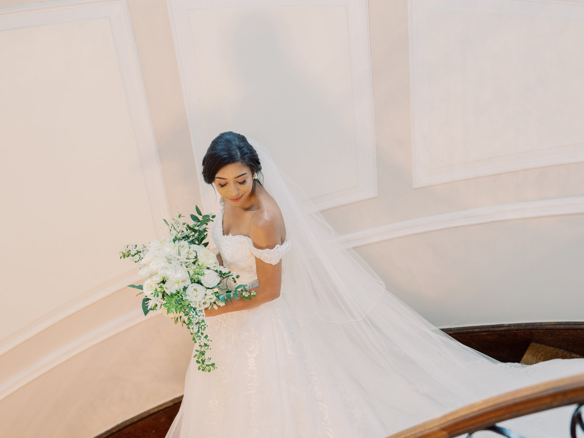 Bride with bouquet walking down a staircase at Oxon Hill Manor