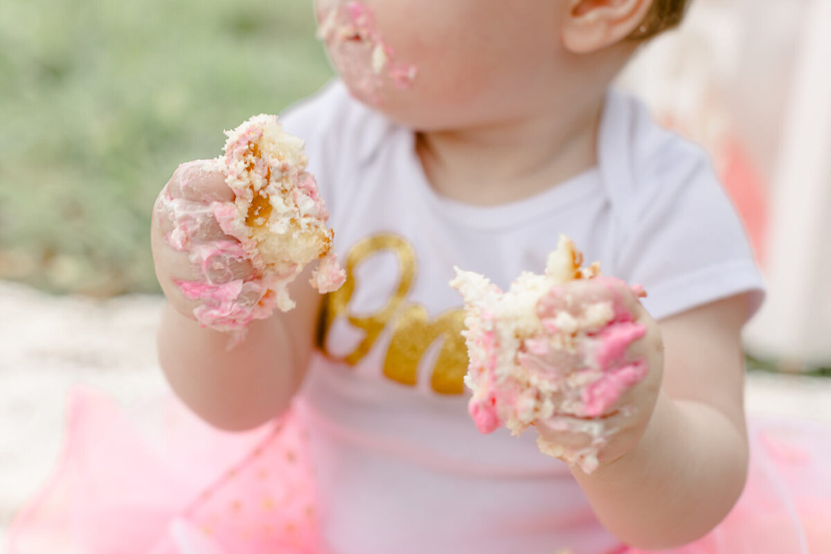 Close up of baby's hands covered in pink cake and frosting during cake smash photo session