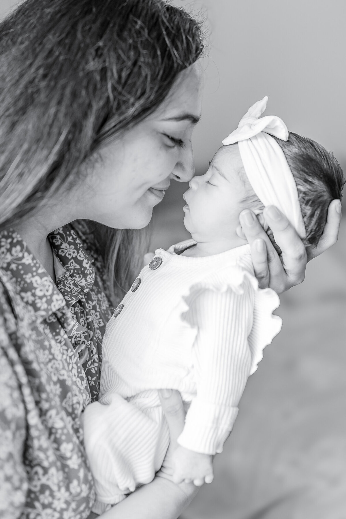 Sweet mother-daughter connection in a soft, natural light newborn photography session. A mom gently cradles her baby girl, sharing an intimate nose-to-nose moment full of love and warmth