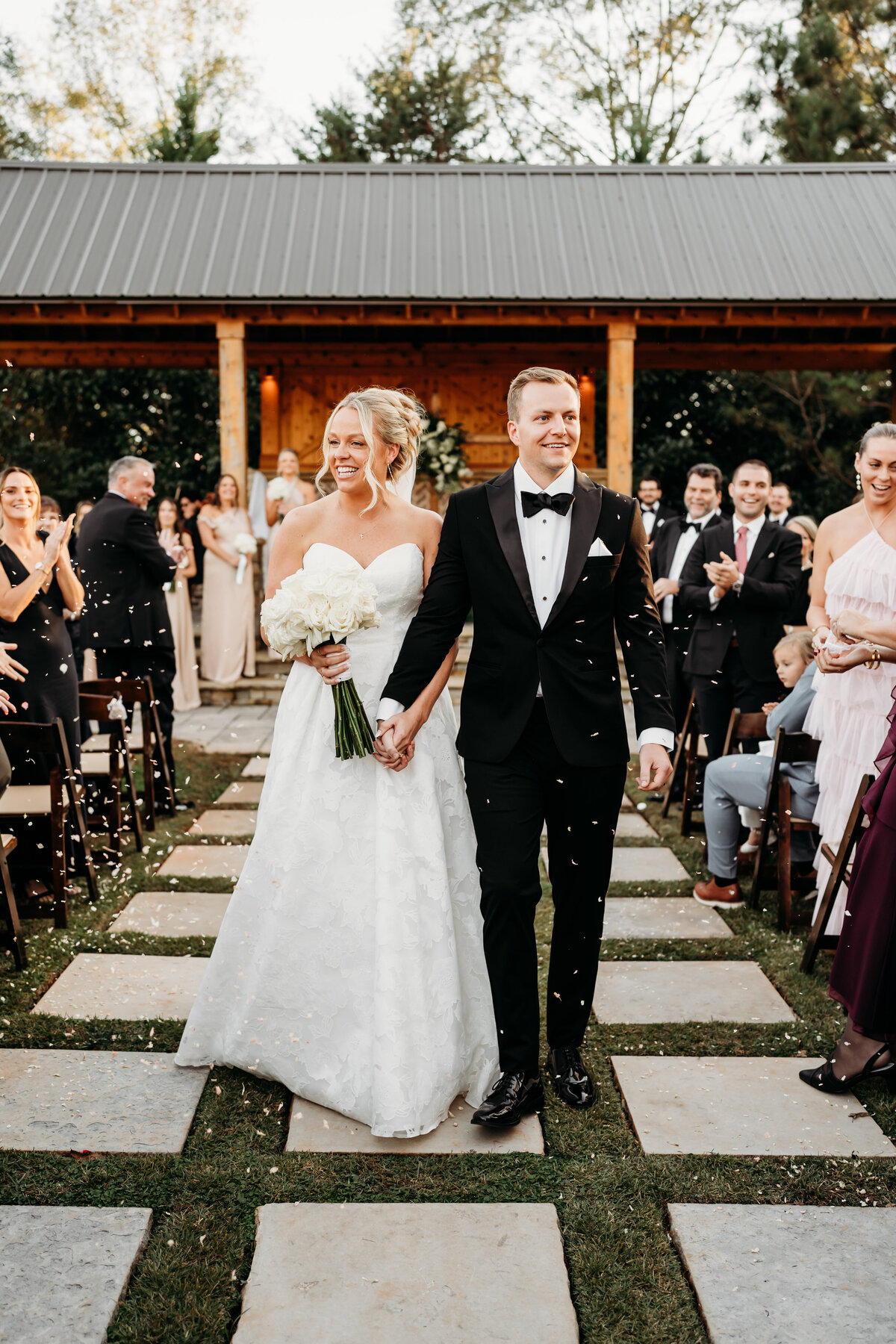 Elegant outdoor wedding ceremony featuring a joyful bride and groom walking down the aisle as newlyweds. Captured in golden light, this stunning moment showcases love, celebration, and timeless wedding style. Perfect inspiration for modern wedding photography and venue ideas.