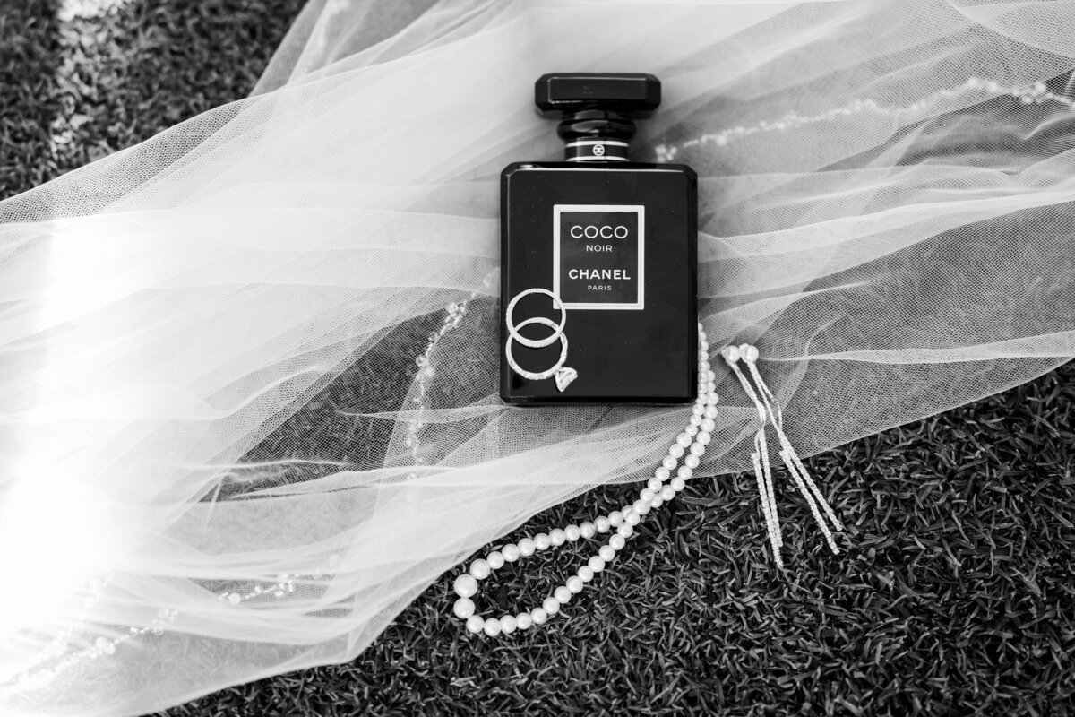 A collection of wedding details including Chanel perfume, a veil, wedding rings, and pearls.