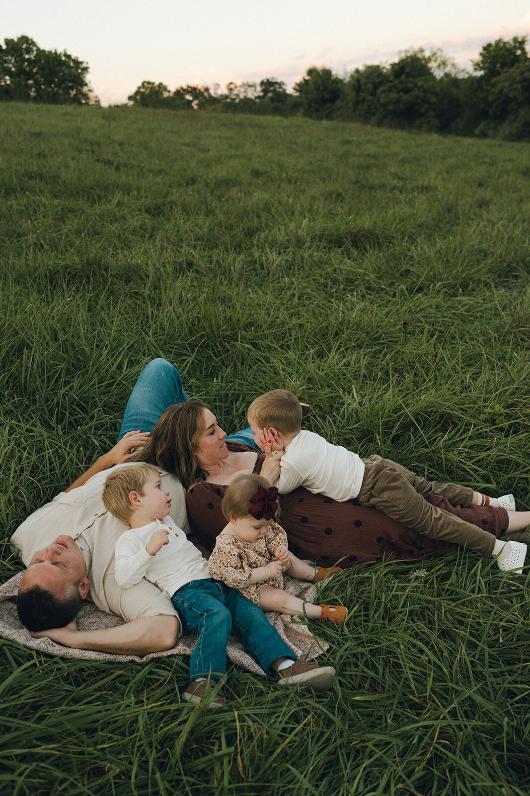 Family of four laying together in a grassy field during a playful, connection-focused photo session