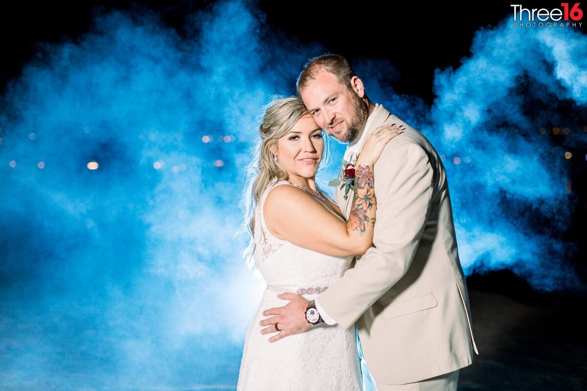 Bride and Groom in a tender moment as they pose for photo with a blue mist behind them