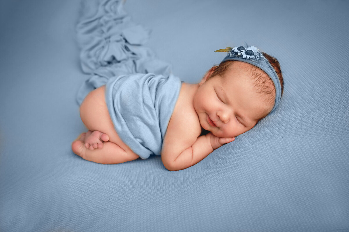 Sleeping infant half wrapped on a blue background at her photo session.