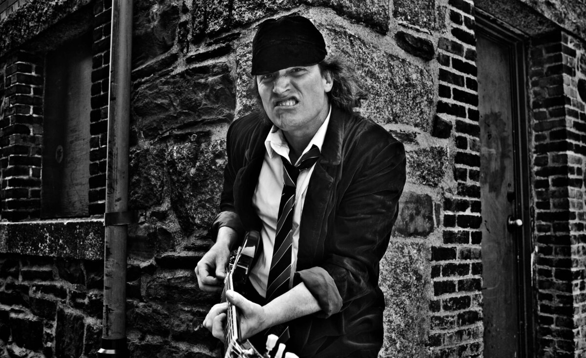 Male musician photo black and white wearing suit with baseball hat playing electric guitar against stone wall background