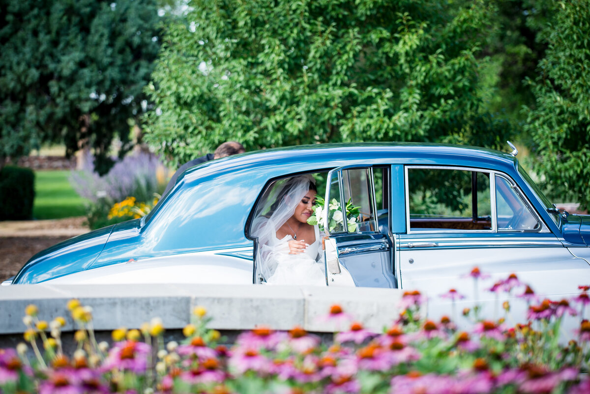 A bride gets steps out of a vintage getaway car with spring flowers in the foreground.