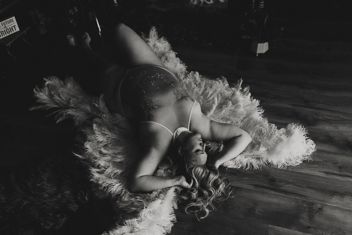 Woman reclines on white shag rug in rhinestone lingerie during high contrast black-and-white boudoir in Jacksonville, Florida.