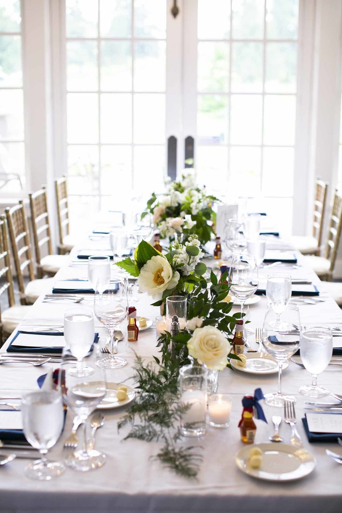 long wedding table lined with centerpieces of white peonies and white roses and greenery and candles