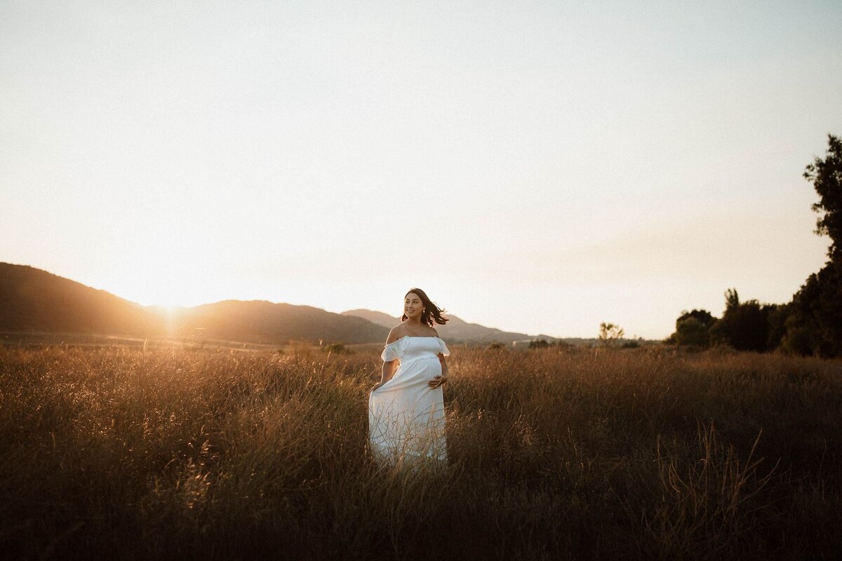 Outdoor maternity session in a wide Temecula field at sunset with glowing golden light.