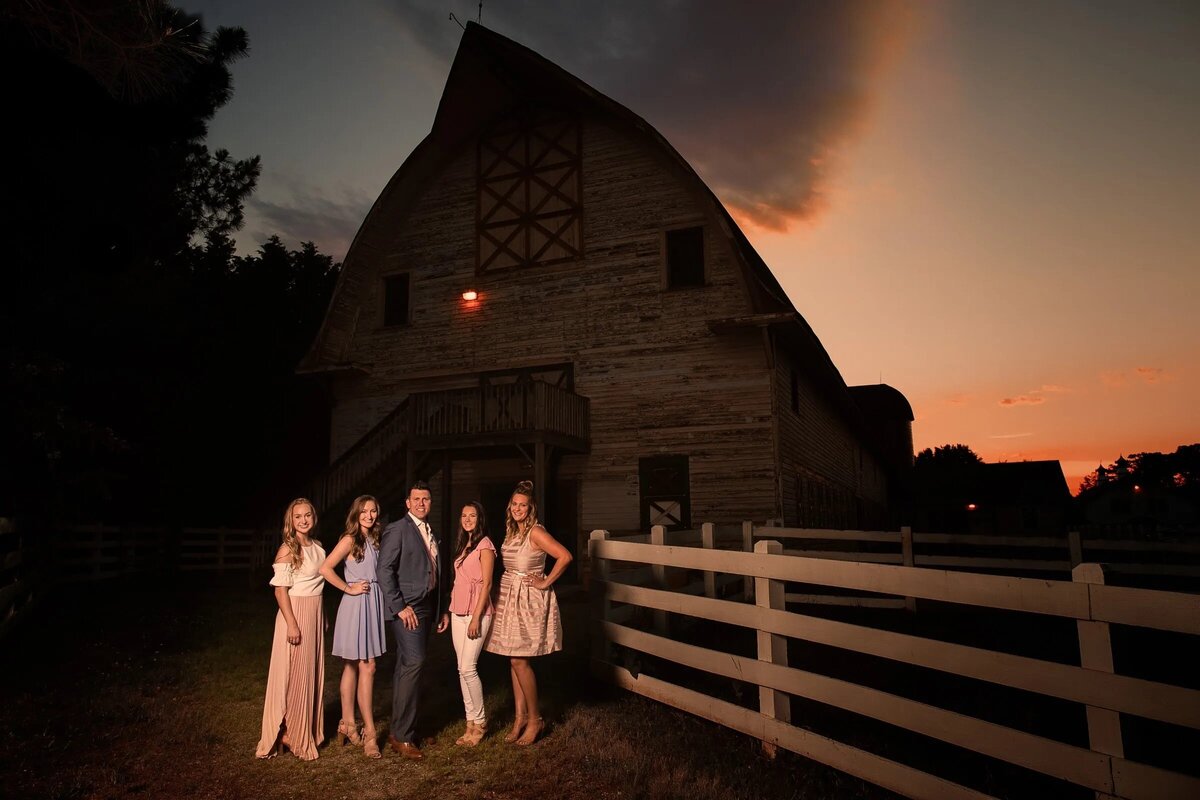 A group of people standing in front of a barn at sunset.