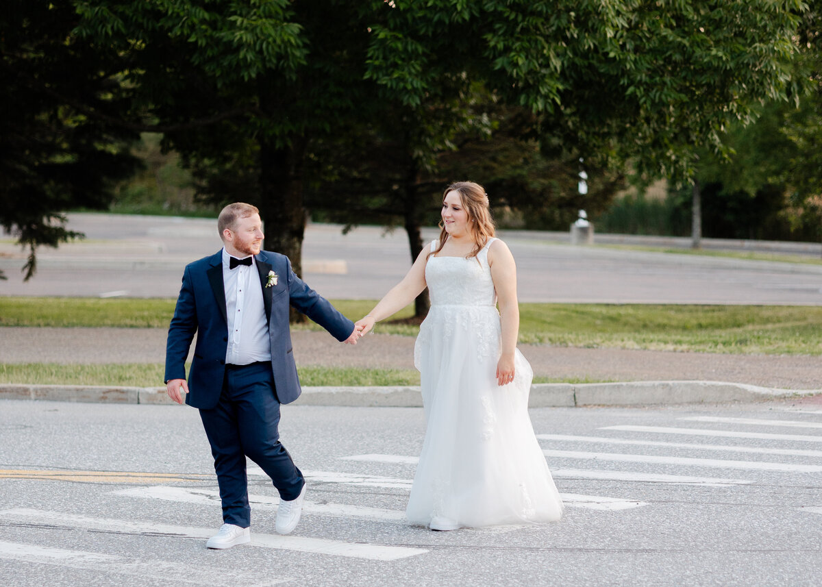 Bride and groom walk hand in hand across the street at sunset