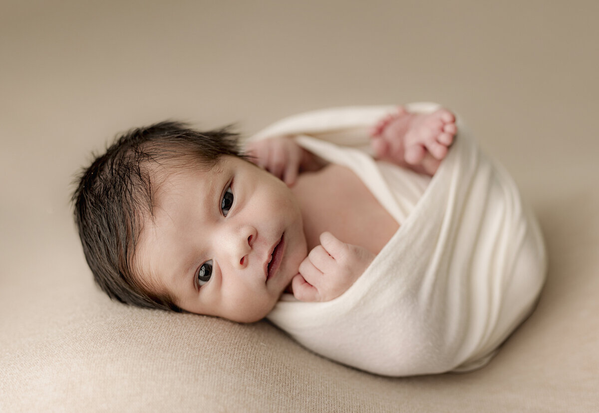 baby wrapped up laying on cream backdrop