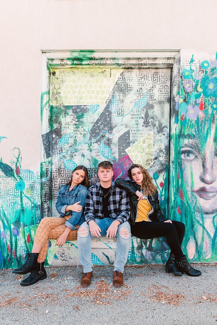 2 senior girls and 1 senior guy seated on doorstep of an painted wall