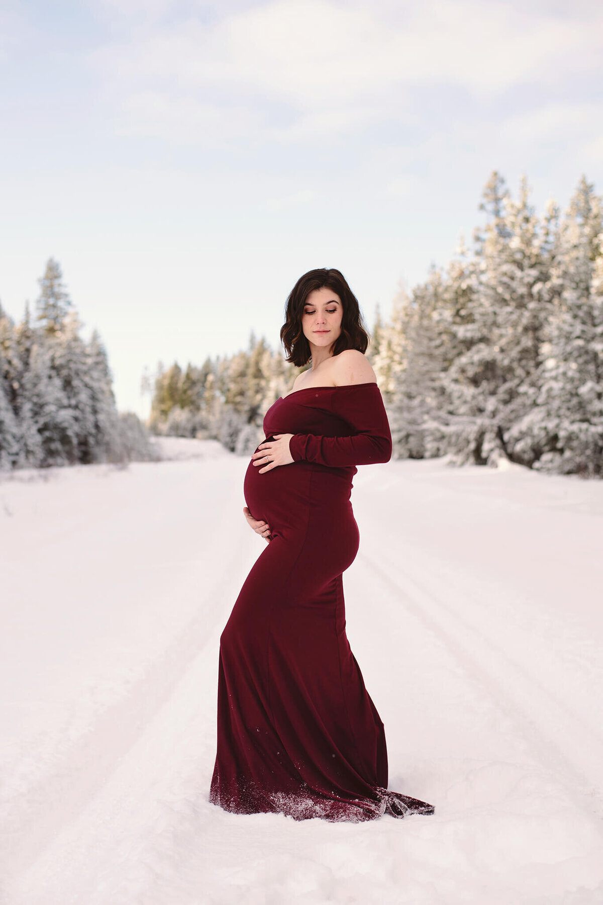 A young women with short brown hair wears a red dress. She is pregnant and it is winter.