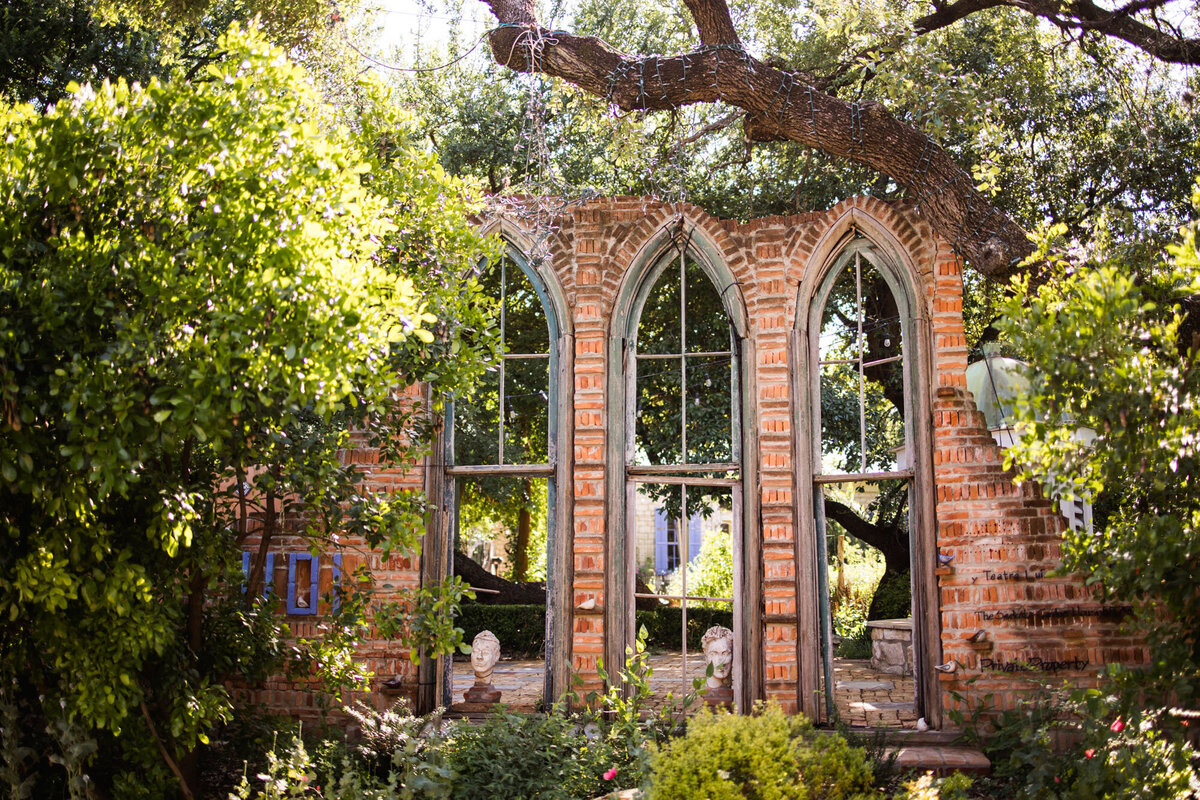Outdoor ceremony site with tall arched windows and trees.