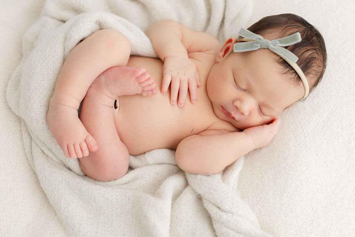 Sweet newborn baby sleeping sweetly all curled up with a beige blanket wrapped around her.