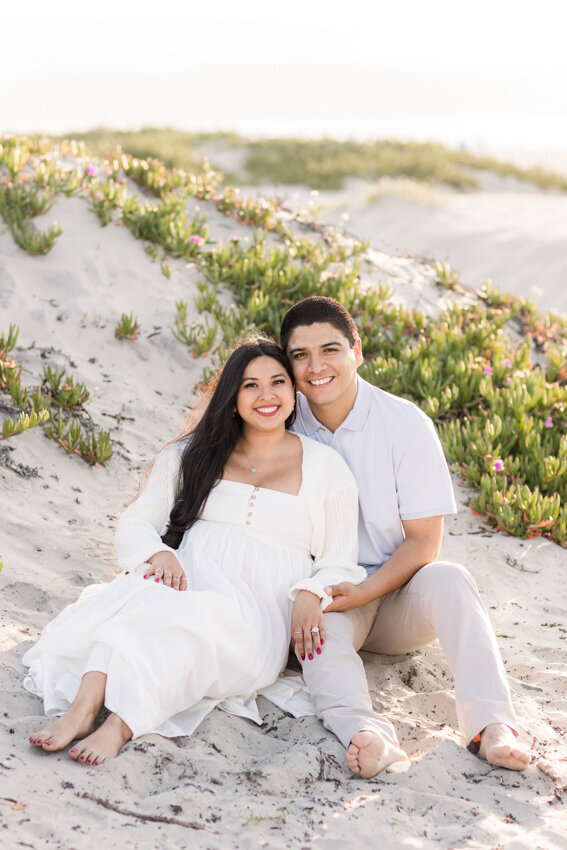 engaged-couple-sitting-in-sand-dune-Coronado-San-Diego