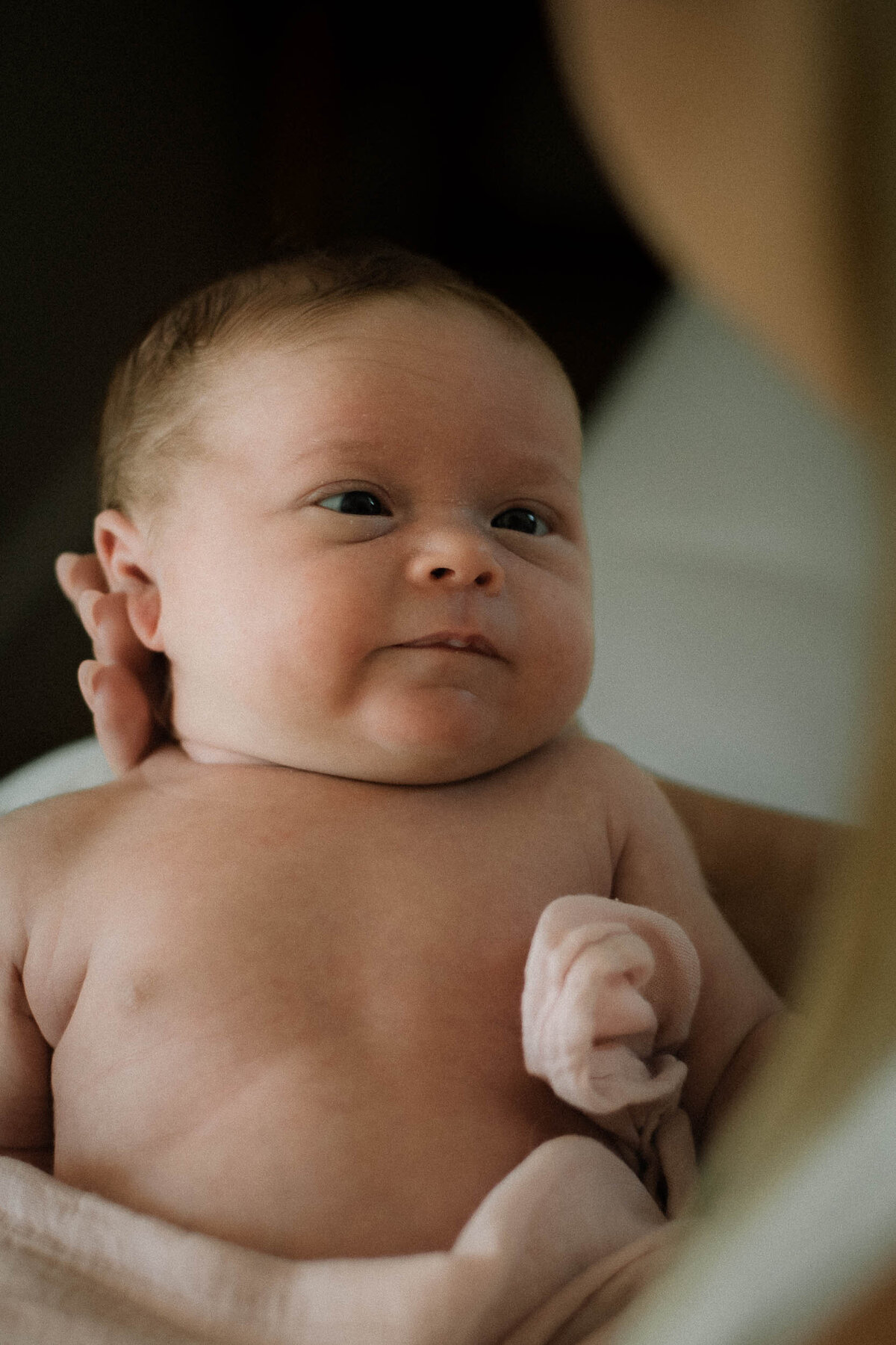 Baby looking at mom with gentle expression while in mom's arms during an Orange County newborn session.