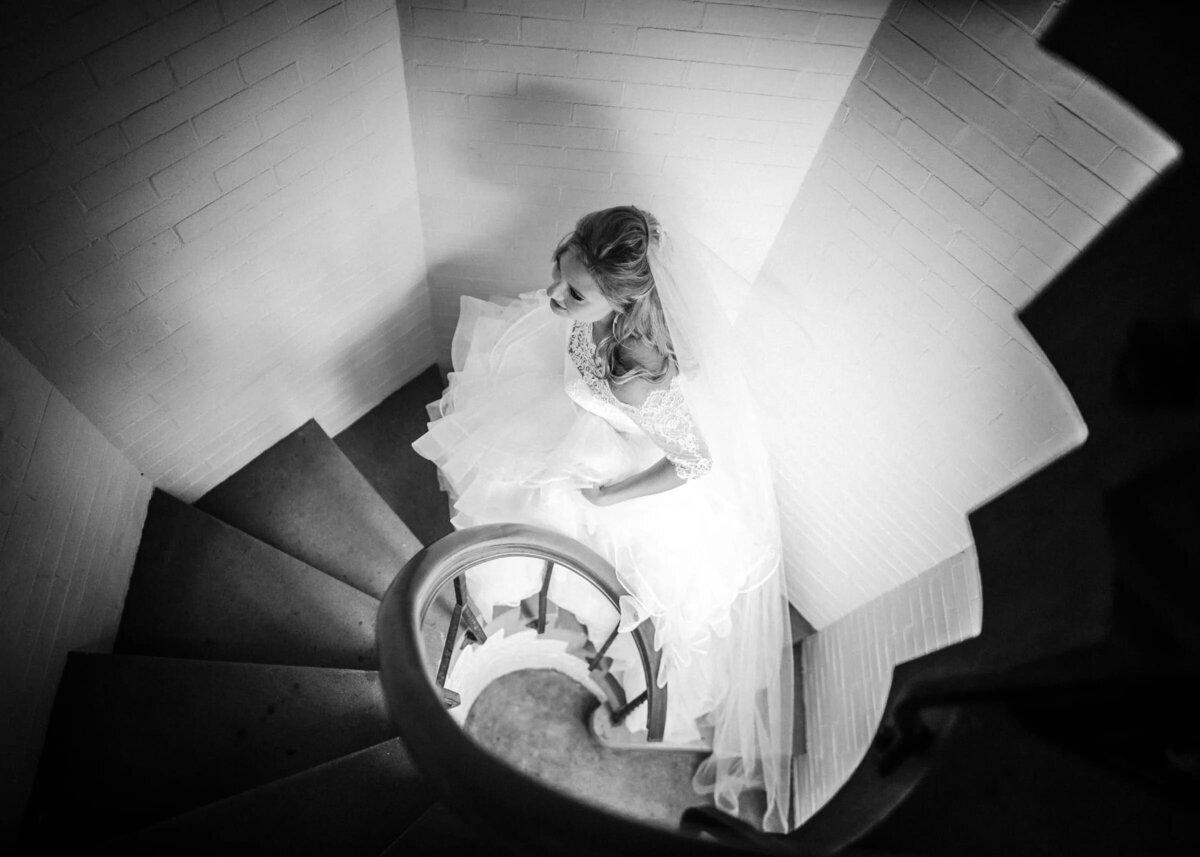 Aerial view of a bride in a flowing dress ascending a spiral staircase