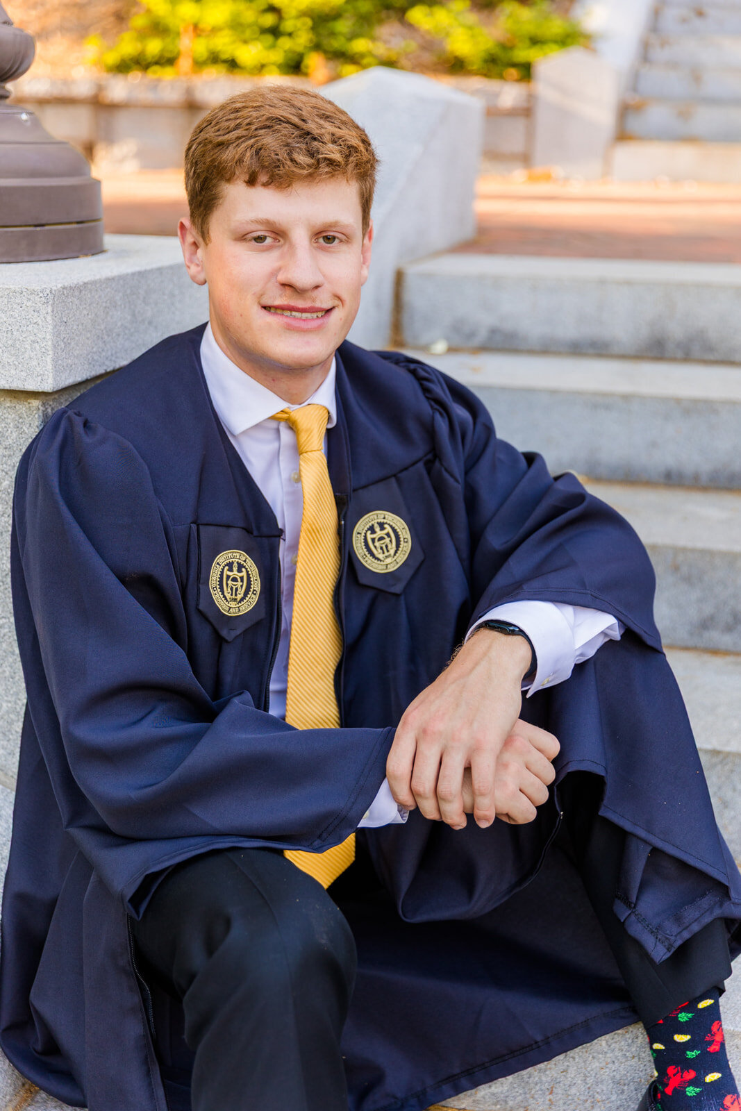 Senior Georgia Tech University student standing on stairs against a low wall wearing graduation gown over a white shirt and a yellow tie during graduation portrait photo session with Atlanta photographer Laure Photography 