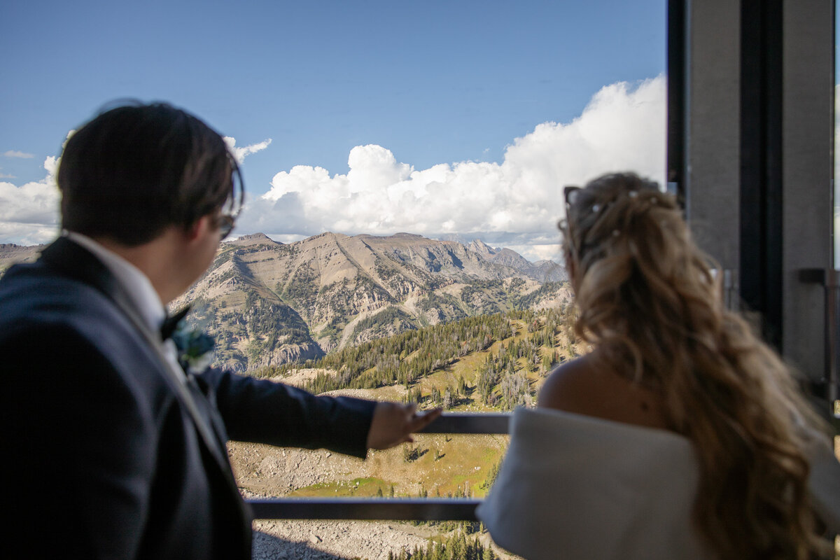 A bride and groom look out the window of a gondola as they ride to the top of the mountain on their elopement day.