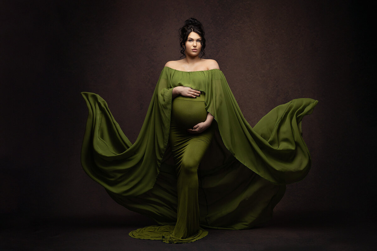 Dallas maternity photography featuring a woman in a flowing green gown with fabric elegantly tossed.