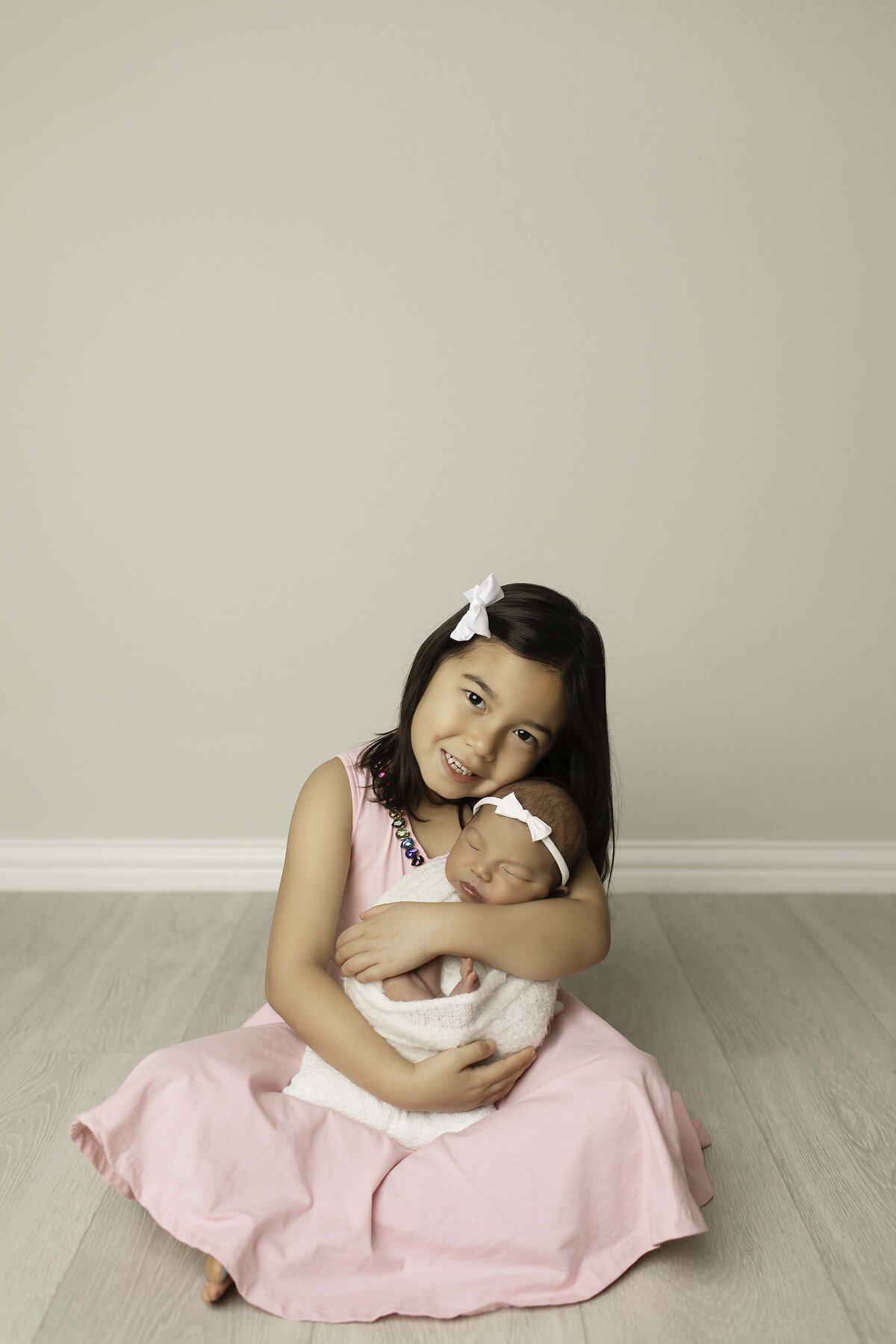 Big sister sitting with her newborn baby brother in her lap, holding him securely with love and care, as she gazes at him with warmth and affection