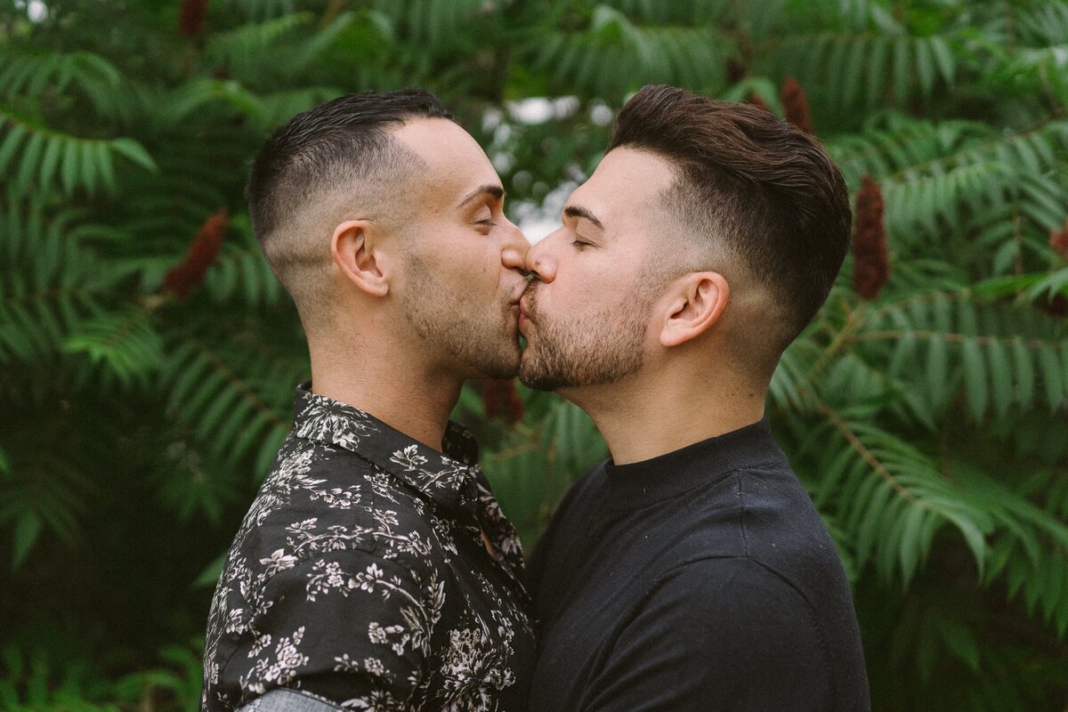 couple kissing in front of green bushes