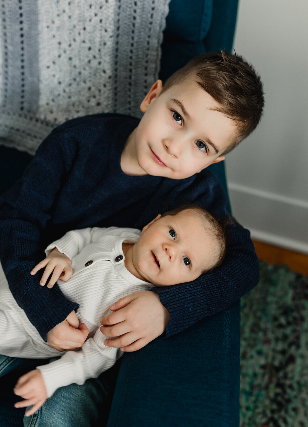 Young child holding newborn baby sitting in a chair.